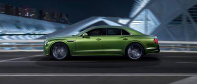 Side profile of the new hybrid Bentley Flying Spur in Tourmaline Green driving in an urban environment